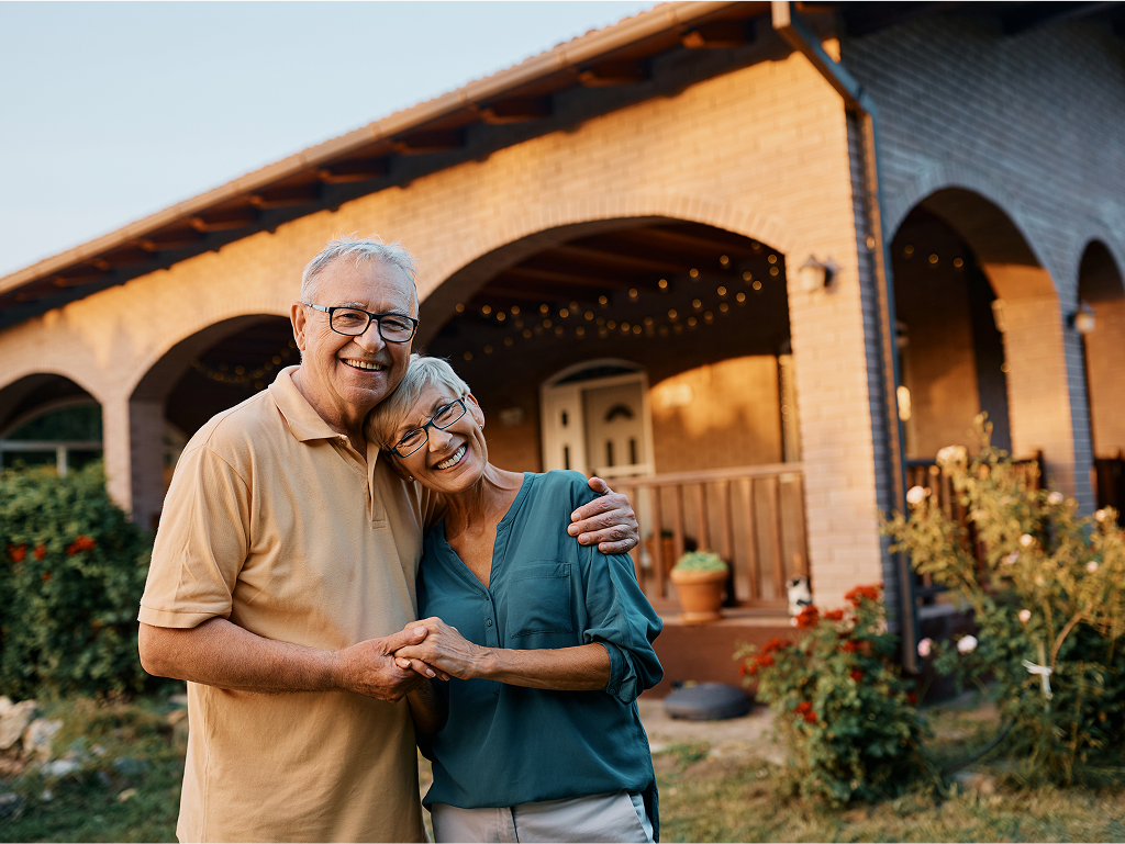 Happy senior couple standing in front of their home, smiling and enjoying a joyful moment together