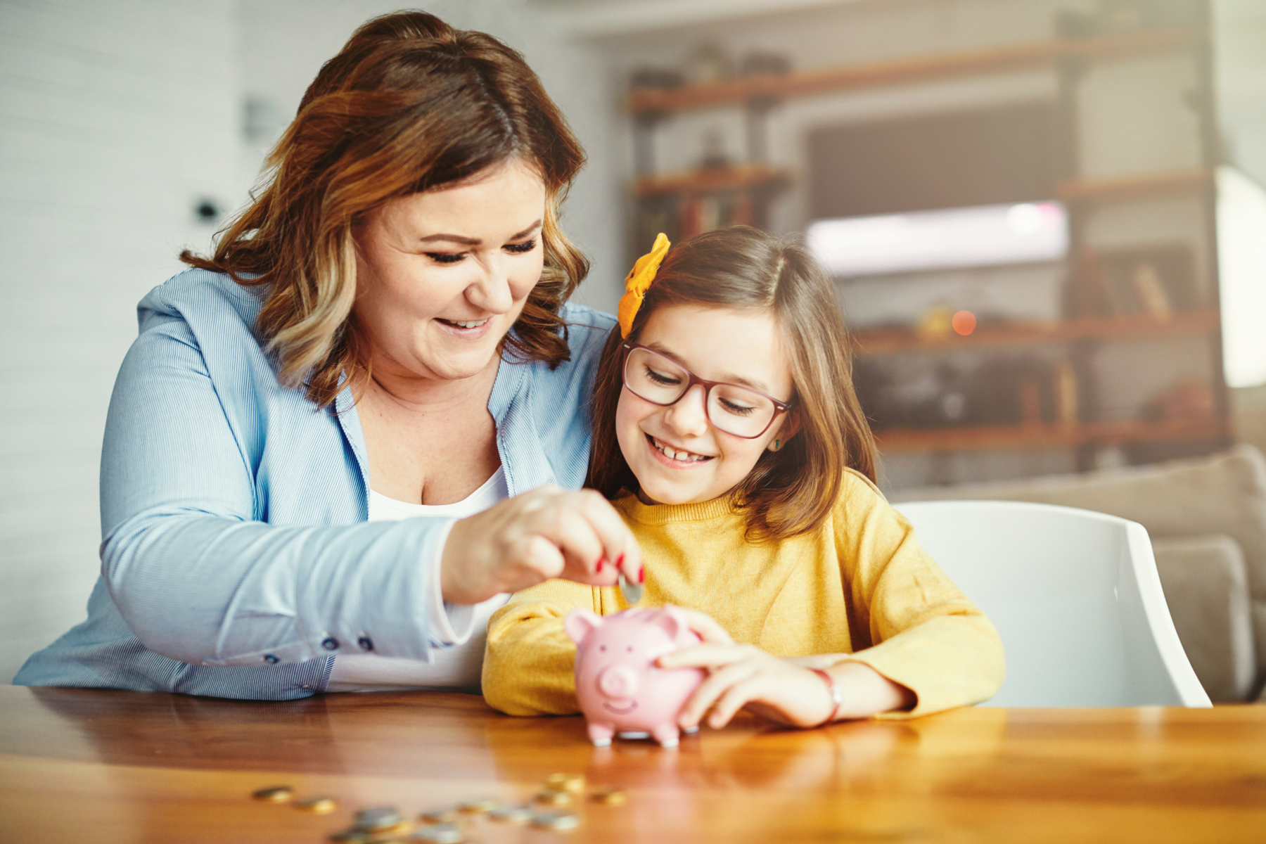 Mother and daughter sitting together, happily saving money in a piggy bank and learning about finances